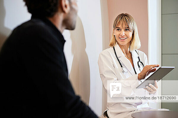 Blond female doctor holding tablet while discussing with male patient