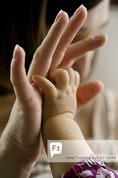 A baby girl reaches up to clasp the hand of her mother in an intimate moment in their California home.