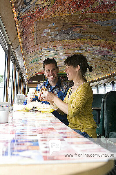 Young man and woman have lunch in restaurant made from old school bus.