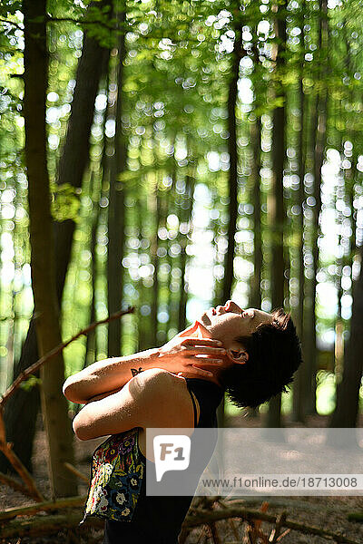 dancer touches face tenderly in sunlit green forrest in Europe