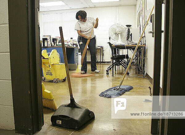 A female janitor sweeps the floor with a broom and dustpan in a historic shopping mall  (low angle).