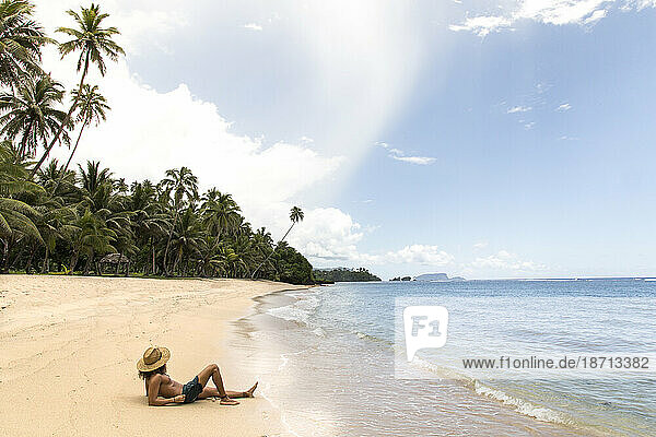 Latin man  wearing straw hat  tanning on golden sandy beach  Samoa