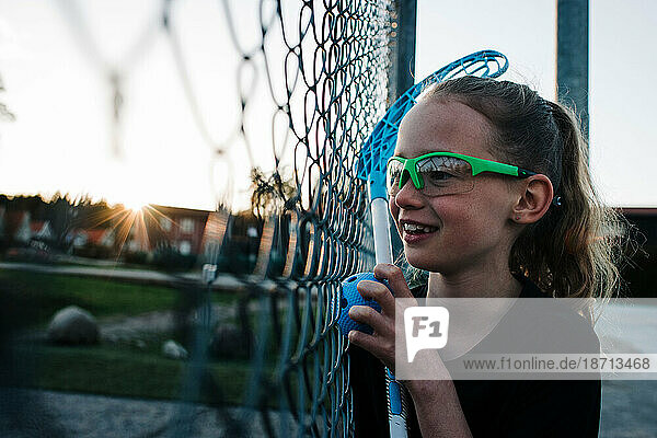 girl looking through a fence ready to plat a game of Innebandy