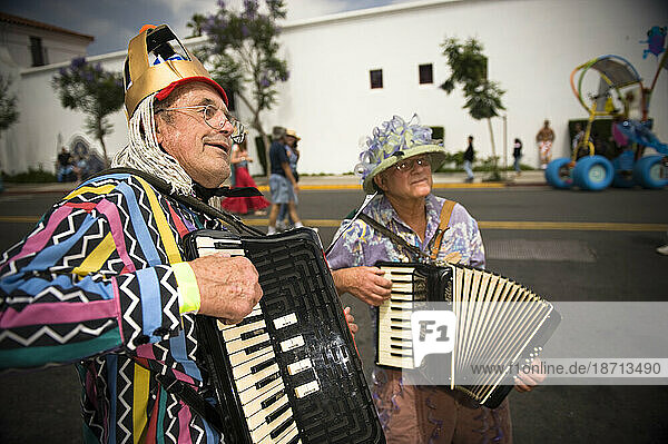 Two elderly men and accordions at a parade in Santa Barbara. The parade features extravagant floats and costumes.