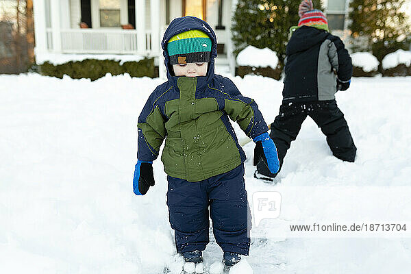 Two boys stand in snow in front yard during winter wearing winter gear