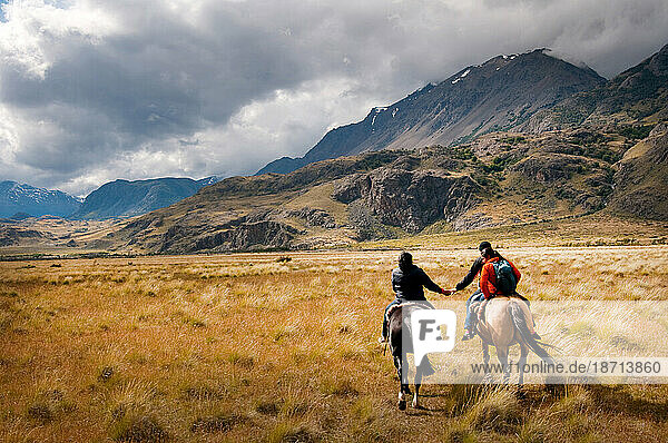 A monther and dayghter hold hands on horse back as they head off to herd sheep on Estancia Chacabuco  Patagonia.