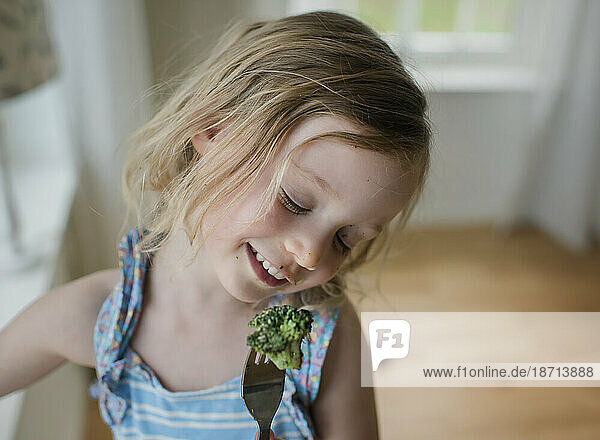 portrait of a young girl eating broccoli with a messy face
