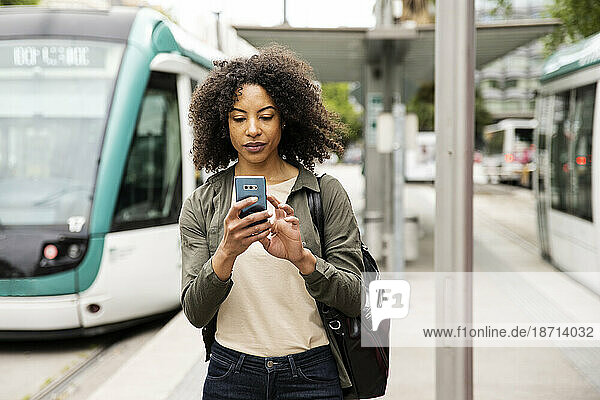 Beautiful relaxed woman texting with his phone on a tramway platform.