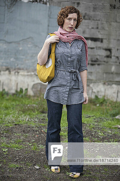 A young stylish woman stands in an empty and overgrown industrial lot in Seattle  Washington.
