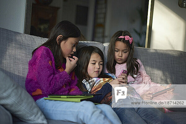 Three young Asian girls on the sofa playing with their tablet at home