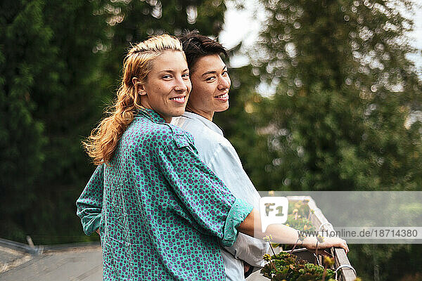 mixed race queer couple stand on balcony with garden smiling
