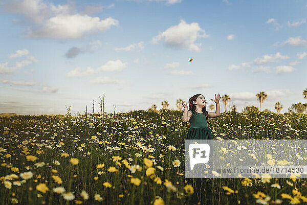 Little girl in dress throwing flowers in field with blue sky