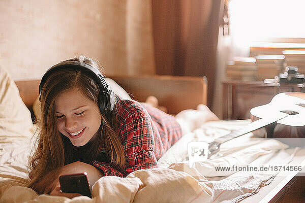 Happy teenager using smart phone while listening music on headphones