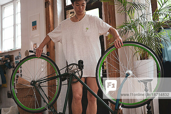 queer woman fixes green vintage bike in wooden studio with plants