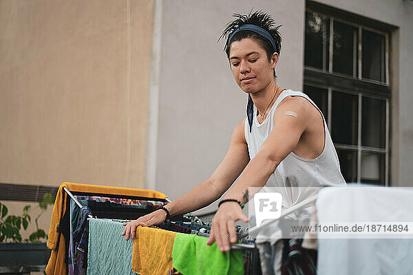 queer asian woman hangs wet laundry on clothes rack outdoors