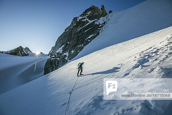 An alpinist tackles a steep snow slope as the sun crests the horizon