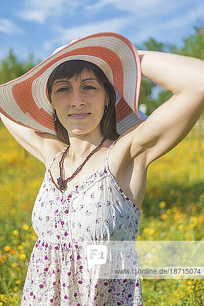 Portrait of young lovely woman wearing straw hat in the flower meadow while looking camera smiling