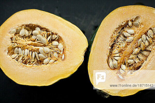 Two halves of an organic acorn squash sit side by side on a black cutting board in a kitchen in Seattle  Washington.