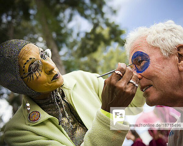 A black woman in costume applies makeup to an elderly man before a annual parade in Santa Barbara.