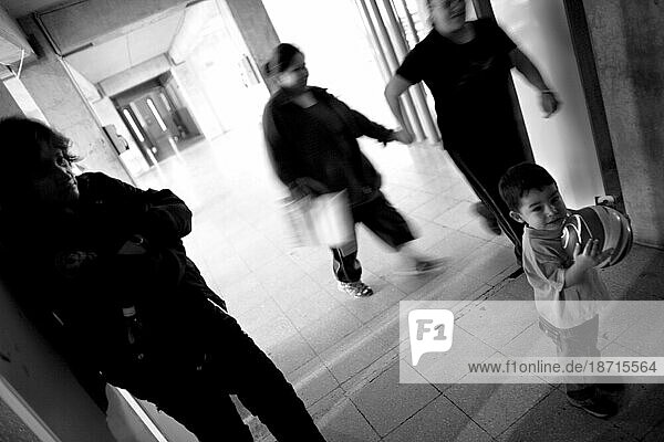 A child plays with a ball in a prison hallway while a guard watches.