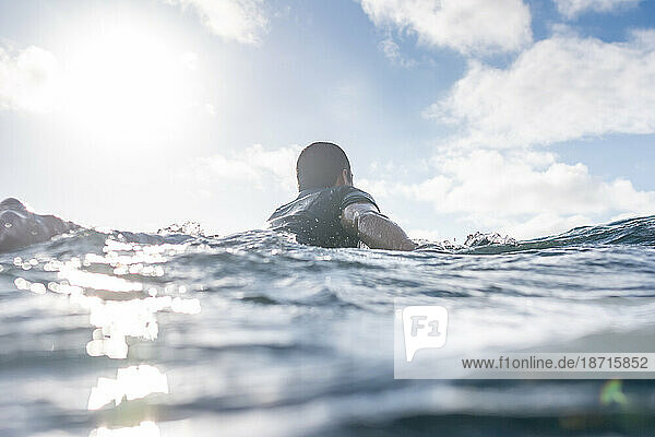 Portrait of surfer man paddling in sea against clear sky