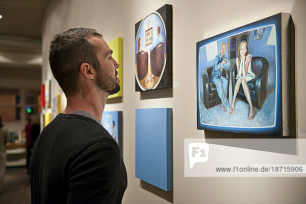 A man takes a close look at paintings in a gallery.