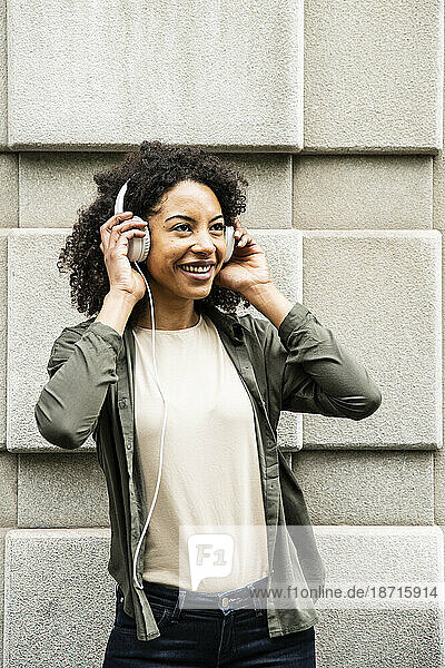 Young woman smiling while using headphones in the street.