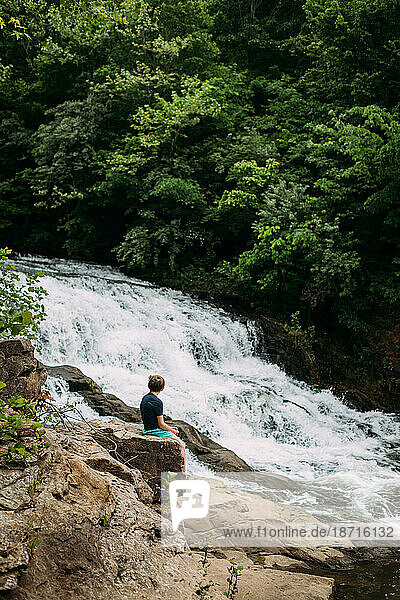 Person sitting on rocks admiring waterfall