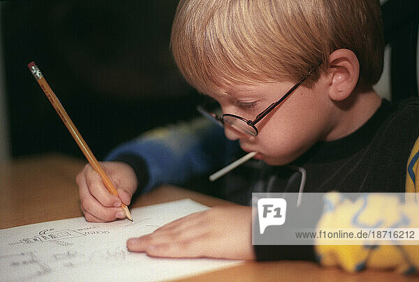 A young boy draws with pencil and paper.