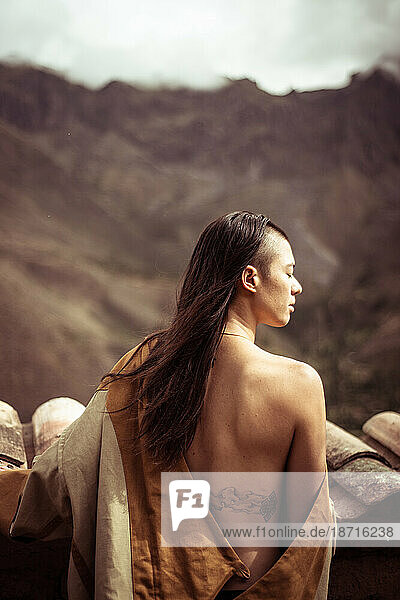 androgynous warrior woman with bare back and tattoo looks at mountains