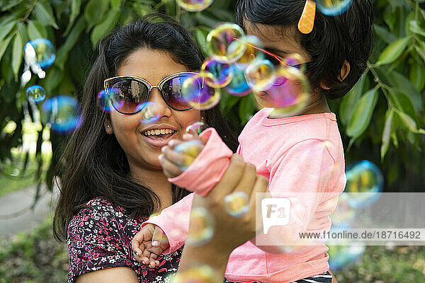 Sisters playing and making fun with soap bubbles at outdoors