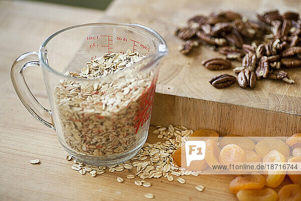 A glass measuring cup or organic rolled oats sits on a counter top with dried apricots and pecans in a kitchen in Seattle  Washington.