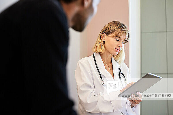 Blond female doctor using tablet PC by male patient in clinic