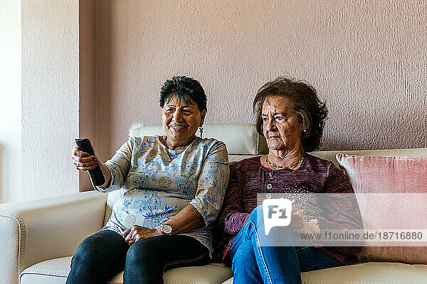 two older modern women watching tv sitting on the sofa