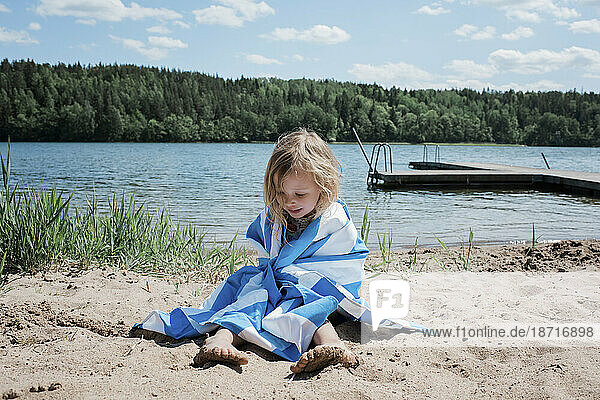 young girl sitting on the beach wrapped in a towel after swimming