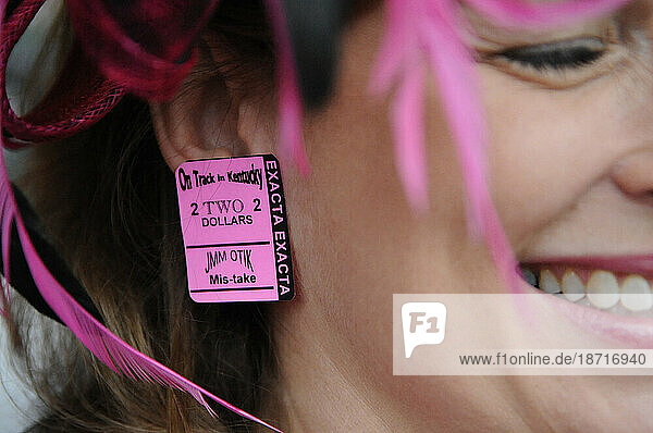 A horse race spectator wears pink commemorative ticket stub earrings to match her pink feather hat.