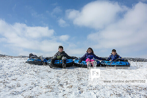 Siblings lined up to sled down a hill smiling and happy