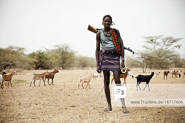 A goat herder pushes his herd through the desert in southern Ethiopia with a rifle on his back.