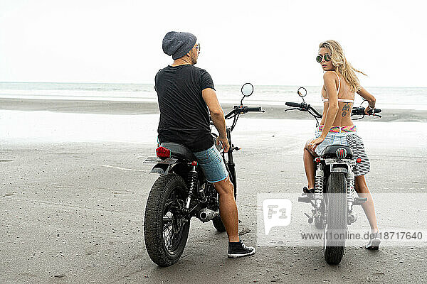 Hipster couple ride a motorcycle on the beach.