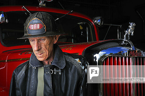A portrait of volunteer firefighter posing in his gear in front of a fire truck.