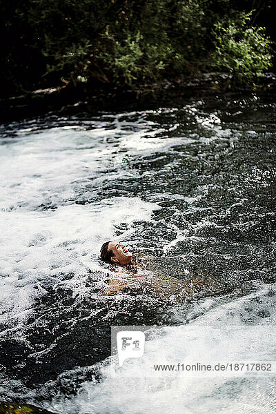 Blond woman bathing in beautiful river waterfall.