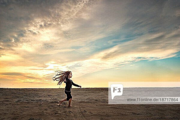 Little girl twirling in the sand at sunset