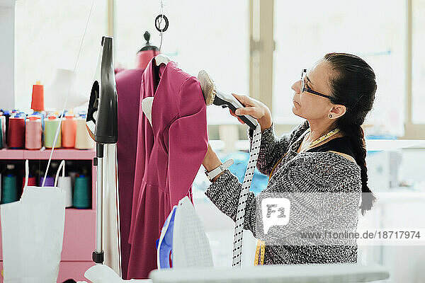senior woman with glasses ironing a dress in a fashion design studio