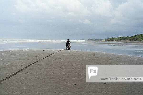 Young man riding a retro motorcycle on the beach.