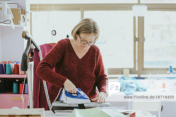 older woman with glasses ironing in a fashion design studio