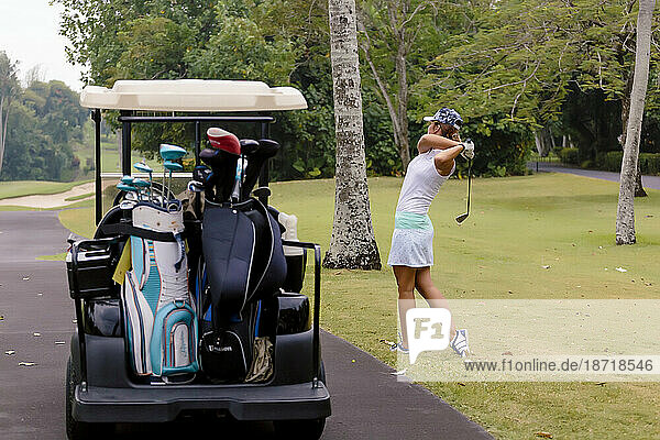 Young woman playing golf by golf cart