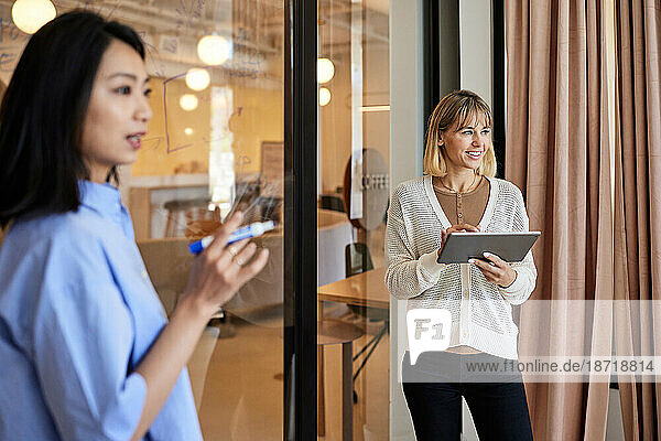 Smiling businesswoman holding tablet PC with female colleague at cafe