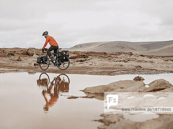 A bike packer is reflected in water on a cold day  Taliouine  Morocco