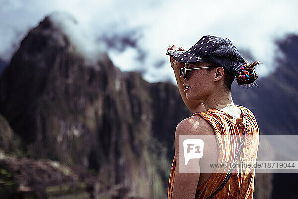 androgynous woman with cap looks at Machu Picchu ruins