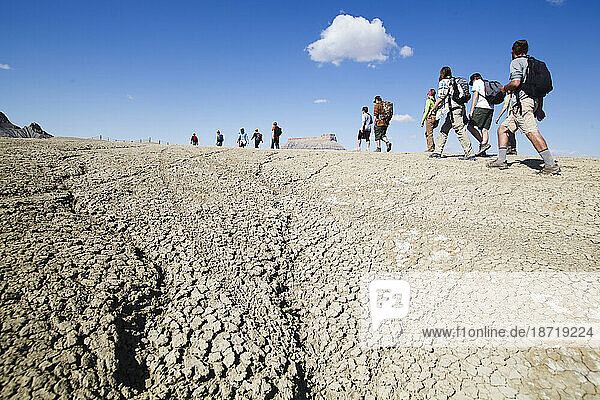 A large group hikes into the mancos shale badlands that surround Factory Butte  Utah.